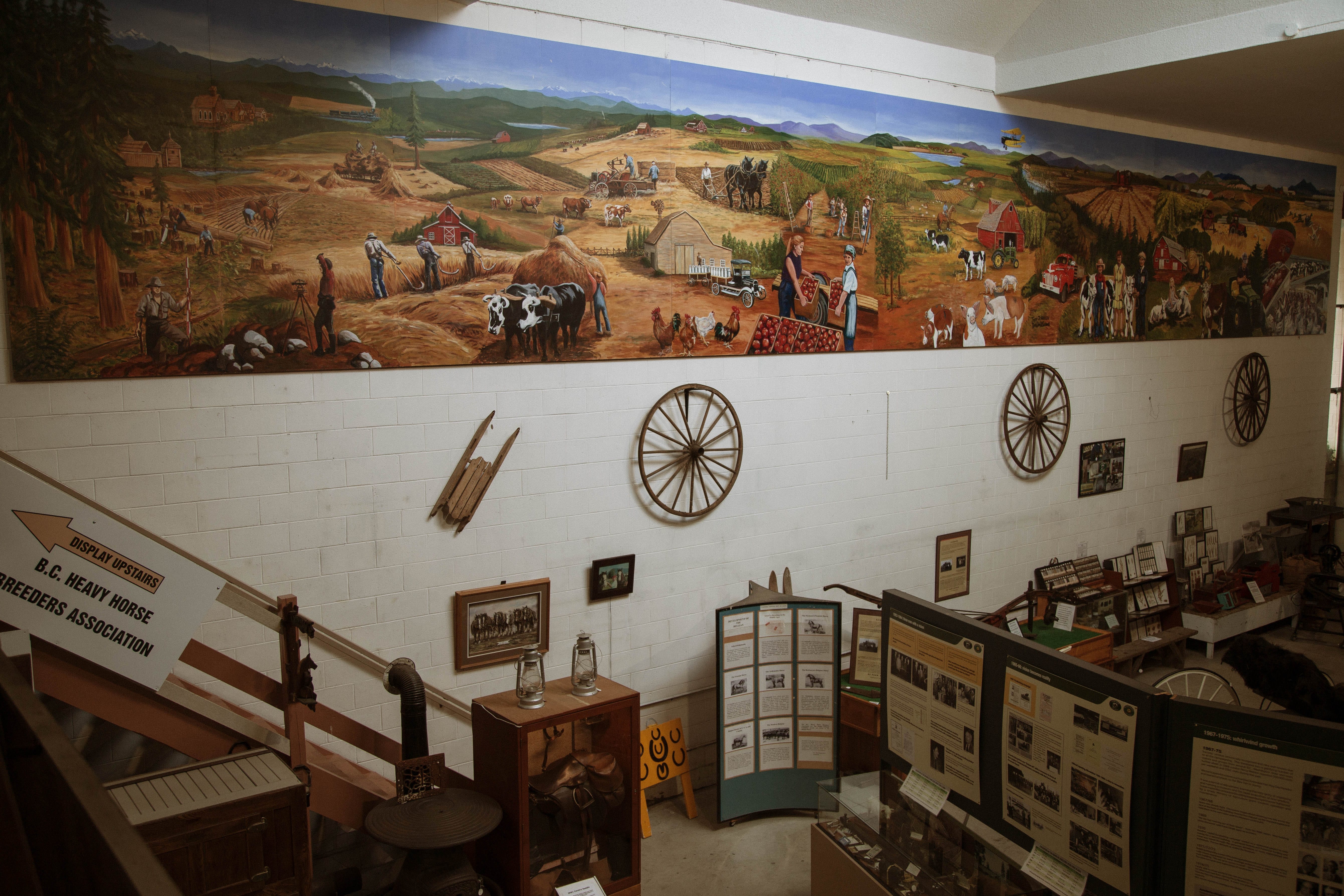A museum exhibit features historical farming equipment, informational displays, and a mural depicting rural farm life and agriculture scenes on the upper wall.