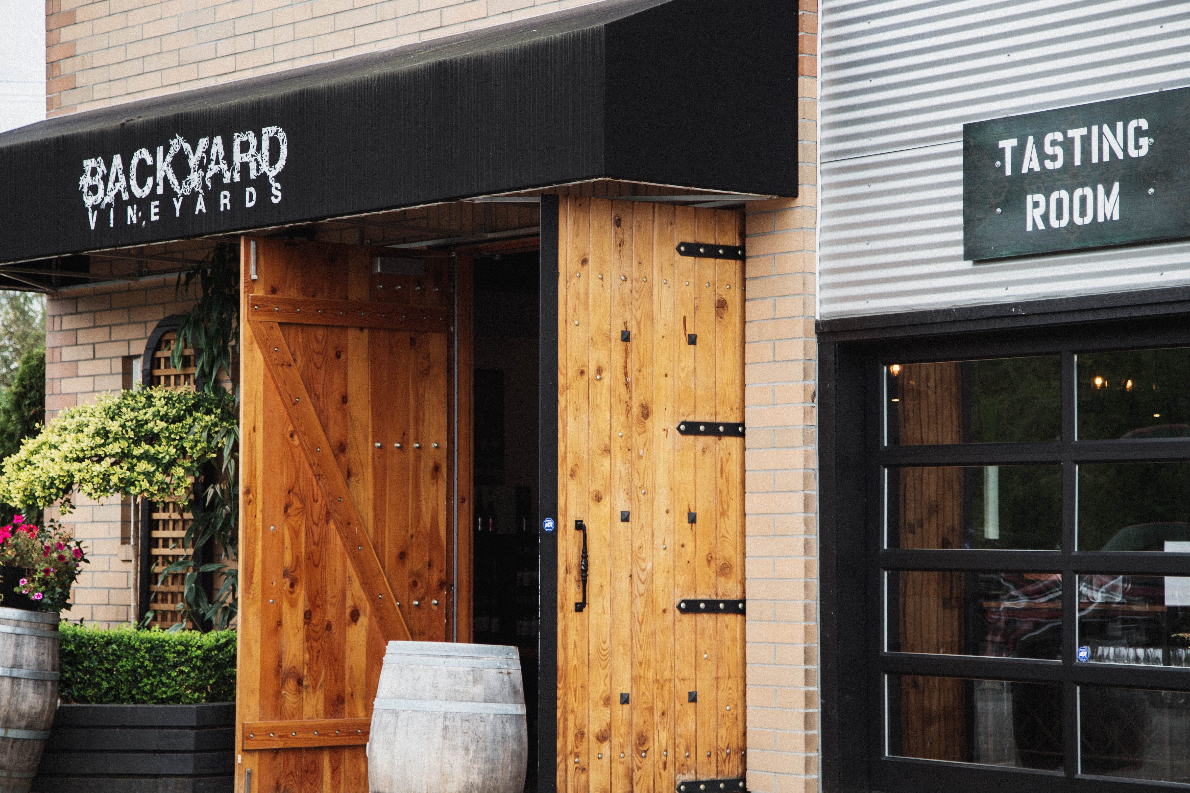 Exterior of Backyard Vineyards with open wooden doors, wine barrels outside, and a sign indicating a tasting room.