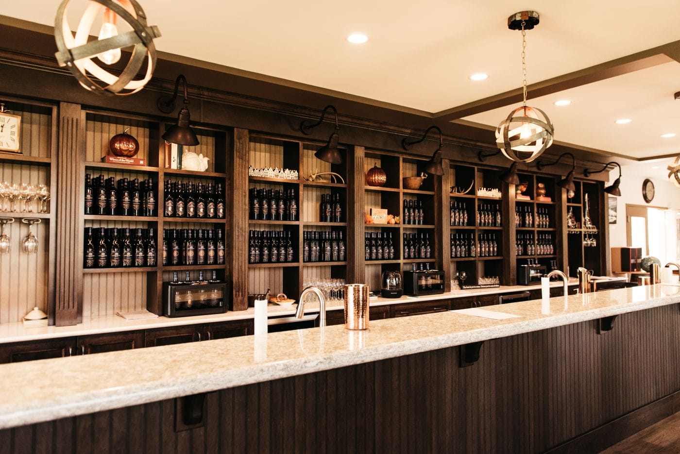 A long bar with a marble countertop, multiple sinks, and shelves stocked with bottles and glassware in a warmly lit room.