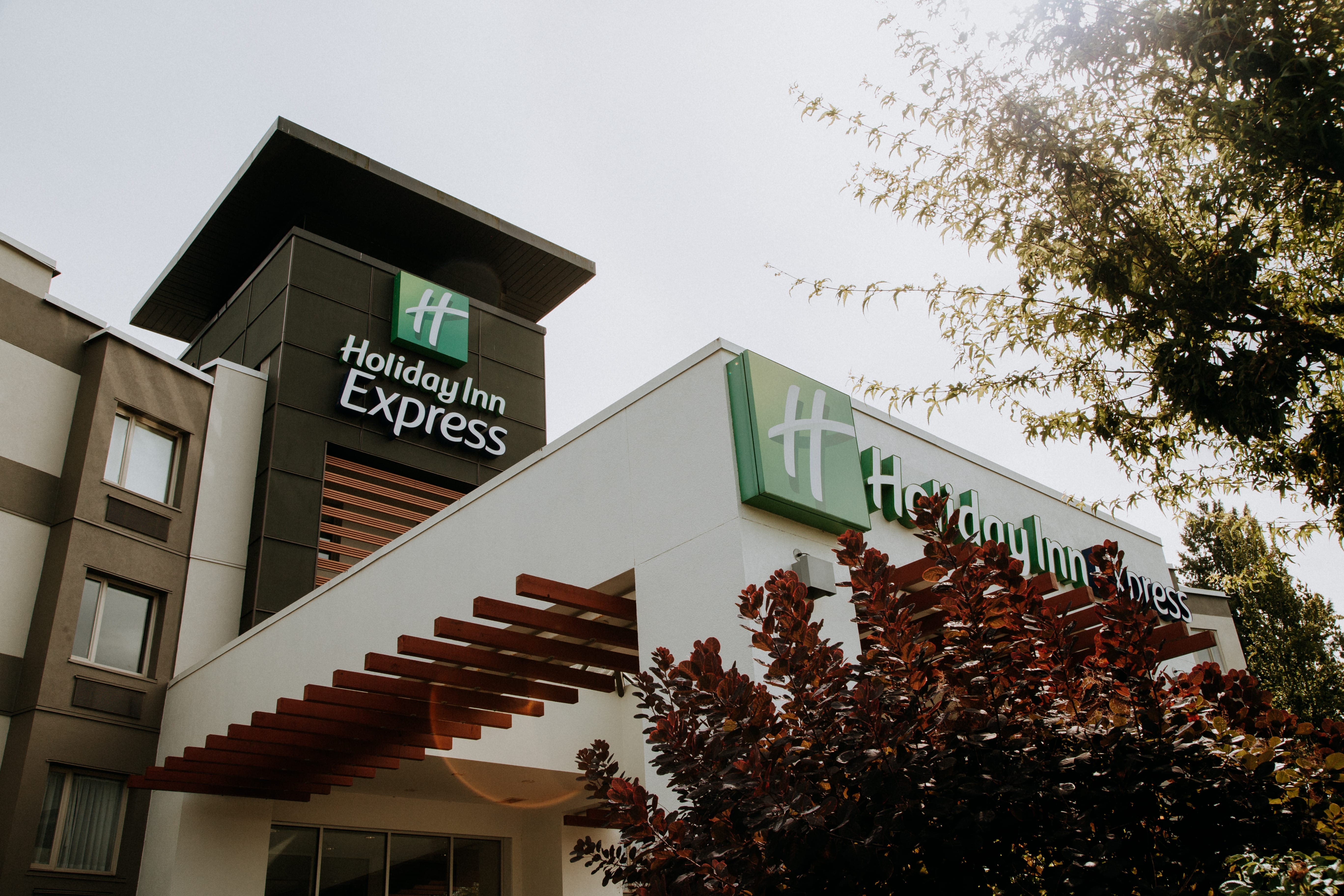 Exterior view of a Holiday Inn Express hotel building, featuring prominent signage and surrounded by trees and landscaping.