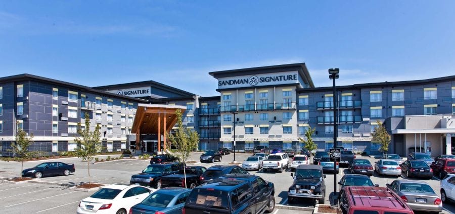 A large Sandman Signature hotel building with modern architecture and a full parking lot under a clear blue sky.