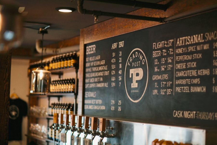 Chalkboard menu displaying beer options, snacks, and flight choices above a row of beer taps in a rustic bar setting.