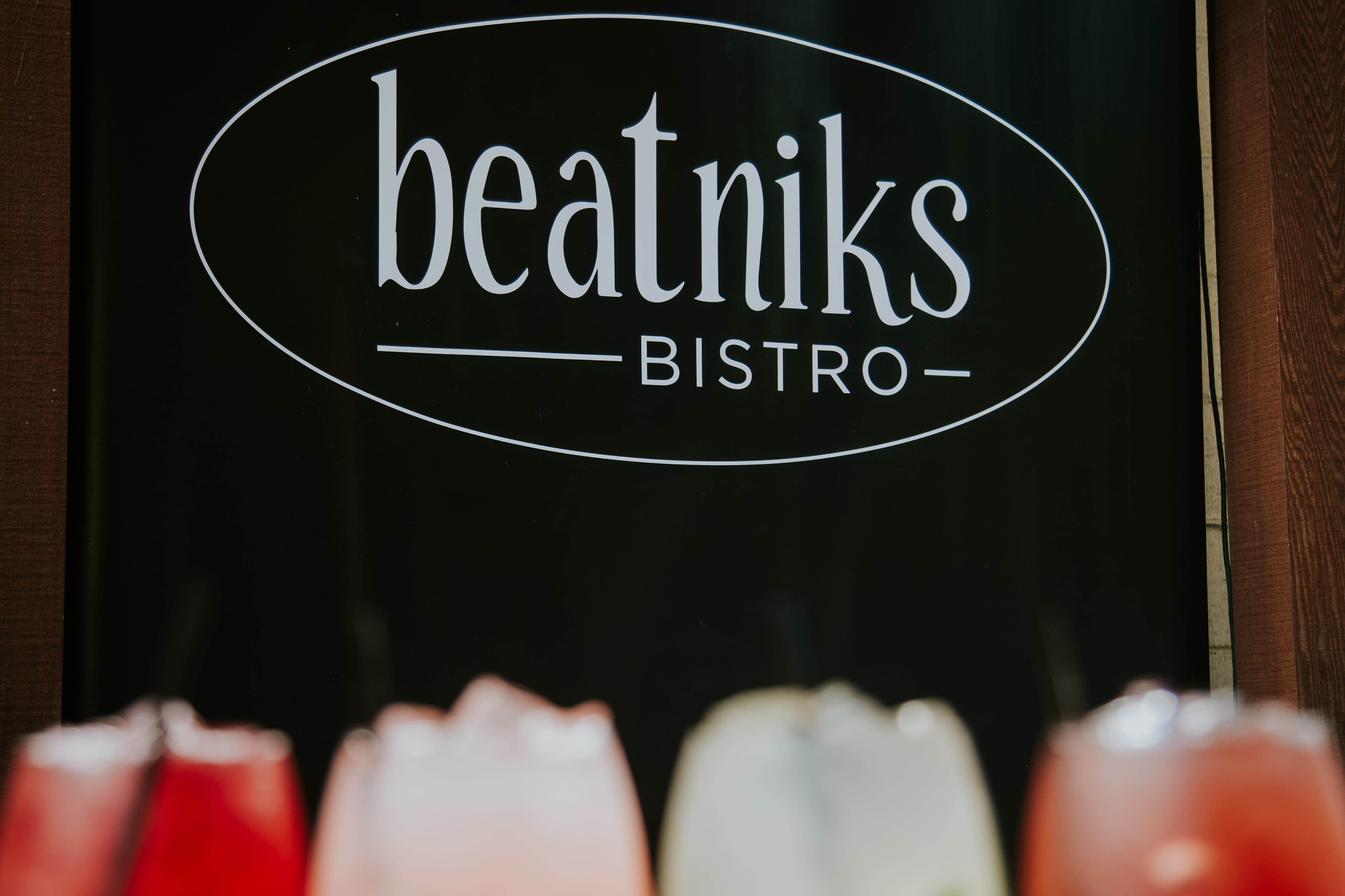 A black sign reads "beatniks BISTRO" in white letters, with blurred colorful drinks in the foreground.
