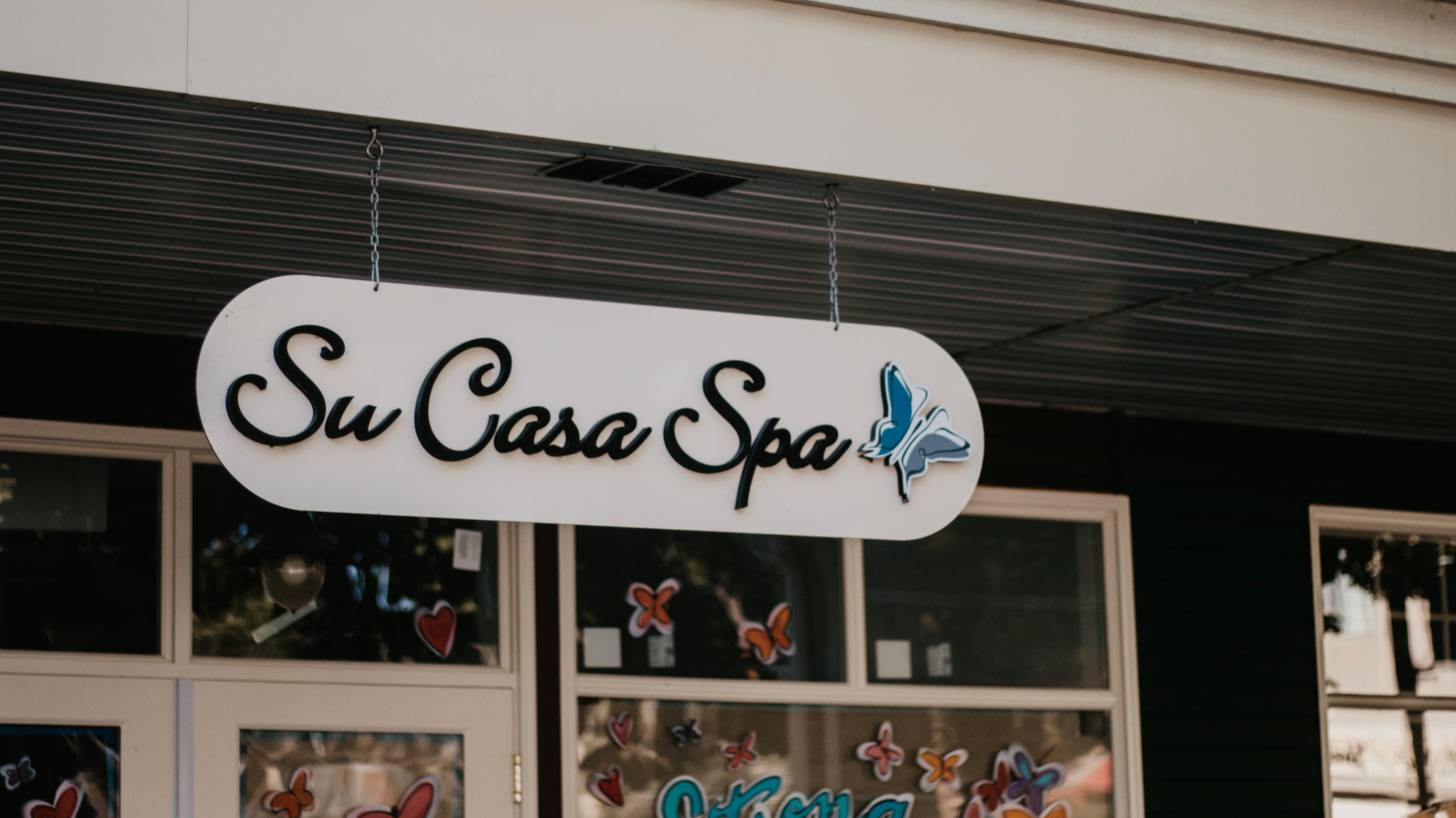 A white sign reading "Su Casa Spa" with a blue butterfly logo hangs outside a building with butterfly decals on the windows.
