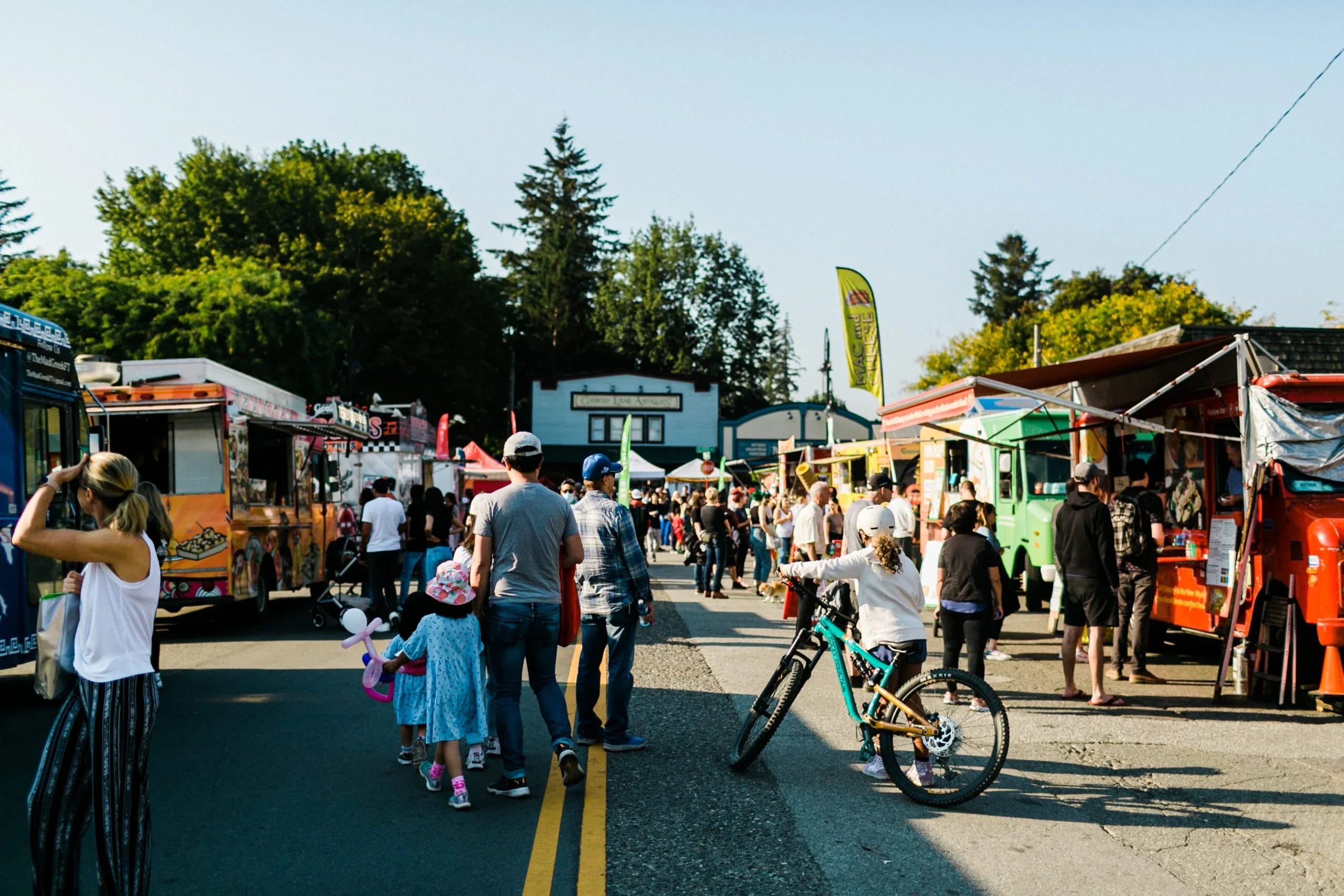 People walk among colorful food trucks lined up on both sides of a street at an outdoor event on a sunny day—a scene straight out of The Ultimate Guide to Langley in the Fall.